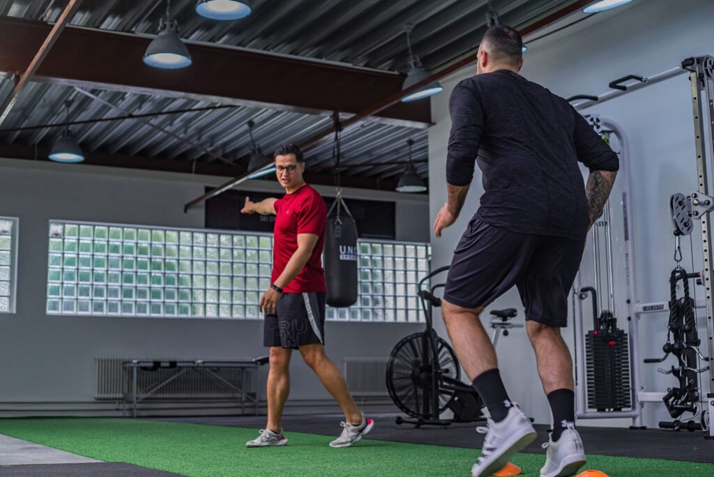 Full body of muscular sportsman in activewear doing exercises with instructor in modern gym
