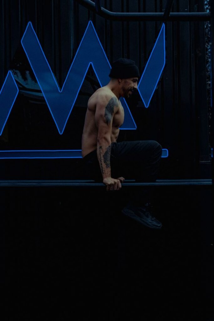 Shirtless, muscular man performing a bar exercise indoors. Fitness focus.